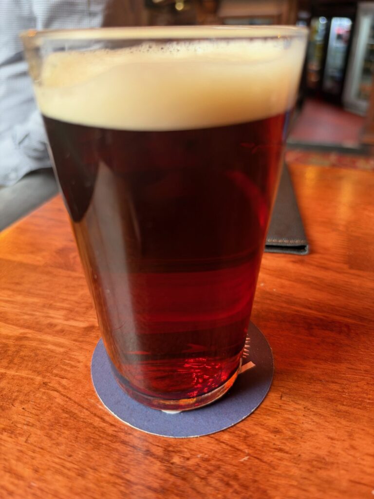 Et glas English Strong Bitter med kobberrød farve og cremet skum på et træbord